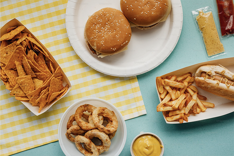 Fast food hamburger, hotdog, fries, and chips on a teal table with checkered napkin