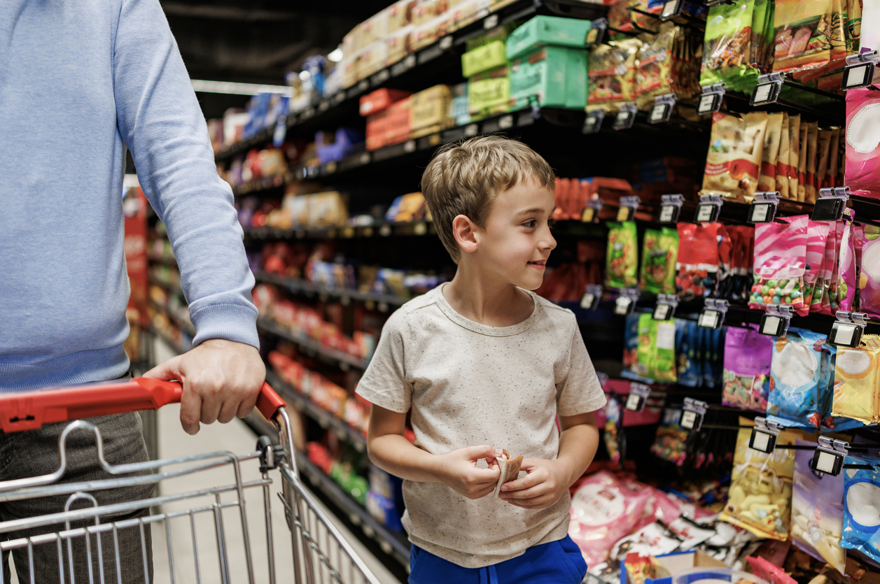Six years old boy walking at the supermarket with his father, choosing groceries and looking around the aisle. iStock Photo Credit: Constantinis